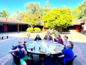 Youth gathered around an outdoor table eating pizza