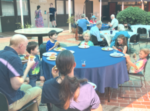 Kids and adults sit around an outdoor table eating a meal.