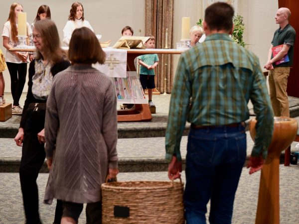 Two people carry forward a basket of offerings at a church service