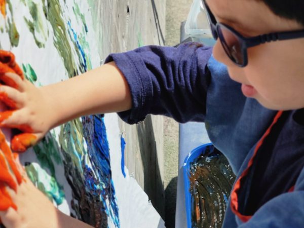 A child whose hands are covered in bright orange finger paint