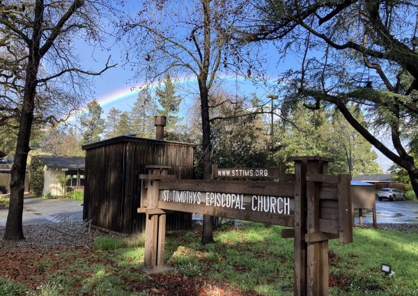 A sign for St. Timothy's Episcopal church underneath a rainbow.