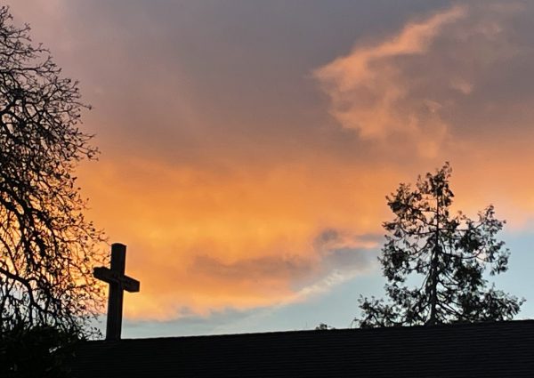 Cross on the roof in front of a sunset sky